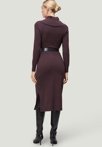 Strick-Midikleid in Dunkelpurpur mit einem breiten, umgeschlagenen Kragen, langen Ärmeln und seitlichen Schlitzen, kombiniert mit kniehohen schwarzen Stiefeln.