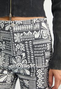 Black and white patterned trousers, featuring geometric designs and accents, made of fabric with a smooth finish. Includes front pockets.
