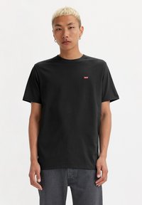 Camiseta de algodón negra con mangas cortas, cuello redondo y pequeño logo rojo en el pecho. Textura suave, corte relajado y diseño sencillo.