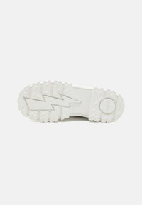 Suela de zapatilla blanca con goma texturizada, que presenta un patrón de zigzag, un logo circular y acentos triangulares elevados para mayor tracción.