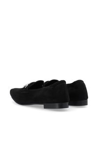 Zapatos de ante negro con suela plana, con una punta redondeada y un detalle decorativo en la parte superior. Textura suave y diseño minimalista.
