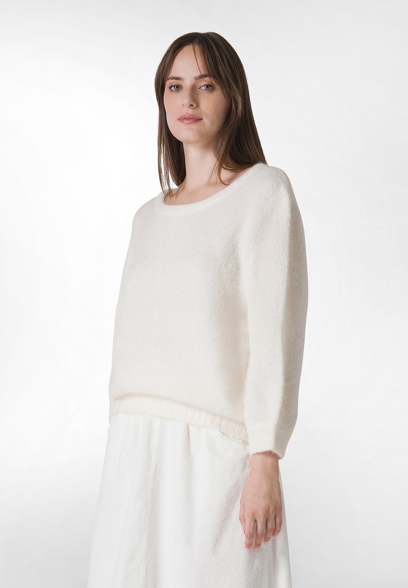 Weißer, weicher, gestrickter Pullover mit rundem Ausschnitt und Dreiviertelärmeln, kombiniert mit einem weißen plissierten Rock.