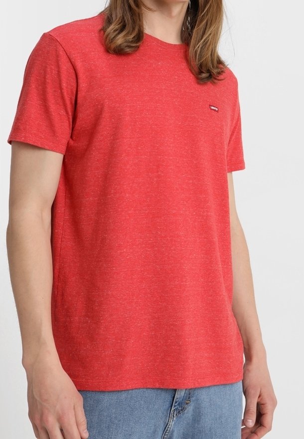 T-shirt rouge à manches courtes en tissu texturé, avec un petit logo sur la poitrine et une coupe décontractée, associé à un jean en denim.