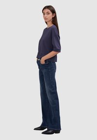 Granatowa bluzka z krótkim rękawem o luźnym kroju, połączona z ciemnymi jeansami dzwonami i czarnymi botkami na szpilce. Minimalistyczny design.
