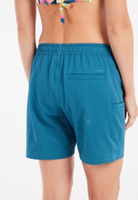 Mėlynos tekstūruotos maudymosi šortai su elastinga juostele ir dviem užpakalinėmis kišenėmis, pasižymintys audiniu raštu. Medžiaga atrodo lengva ir kvėpuojanti.