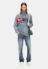 Lichtblauwe denim sweatshirt met een rode grafische logo, versleten details en een geribbelde zoom. Gecombineerd met vervaagde blauwe jeans en witte sneakers.