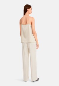 Helles beiges Satin-Camisole mit dünnen Trägern, kombiniert mit cremefarbenen, hochtaillierten weitem Hosen, die eine glatte Textur und ein minimales Design aufweisen.