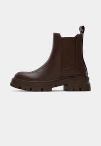 Bruine leren Chelsea-boot met een stevige zool, elasta-zie zijkanten en een trekband aan de achterkant, weergegeven in profiel tegen een witte achtergrond.