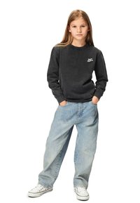 Mustassa pitkähihaisessa hupparissa on pieni valkoinen brändilogo rinnassa. Huppari on yhdistetty väljään vaaleansiniseen farkkuhousuun ja valkoisiin lenkkareihin.