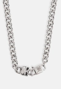 Zilveren ketting met grote schakels, voorzien van een doodshoofdsluiting en gegraveerde hardware voor een veilige sluiting. Gladde metalen textuur overal.