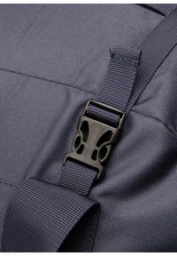 Mørkeblå stof af en rygsæk med struktureret overflade. Har en sort plastikspænde og forstærkede stropper for øget holdbarhed.