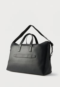 Geantă de voiaj neagră cu textură mată și fină, două mânere superioare, curea de umăr reglabilă și închidere centrală cu fermoar.