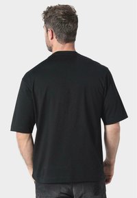 Camiseta de algodón negra de manga corta, con cuello redondo y un ajuste relajado. La vista trasera muestra una tela lisa sin patrones ni logotipos visibles.