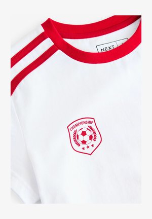 Weiße Baumwoll-T-Shirt mit rotem Kragen und Schulterstreifen. Gesticktes Schild-Logo mit einem Fußball und dem Text "CHAMPIONSHIP".