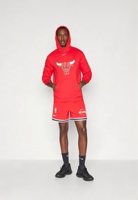 Sweatshirt vermelha com capuz e logótipo dos Chicago Bulls, combinada com calções vermelhos. Detalhes em preto nos calções e ténis pretos. Tecido macio, corte atlético.