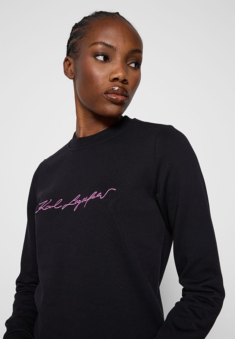 Schwarzer Langarm-Sweatshirt mit lila gesticktem Text auf der Brust. Das Material wirkt strukturiert und hat ein Rundhalsausschnitt-Design.
