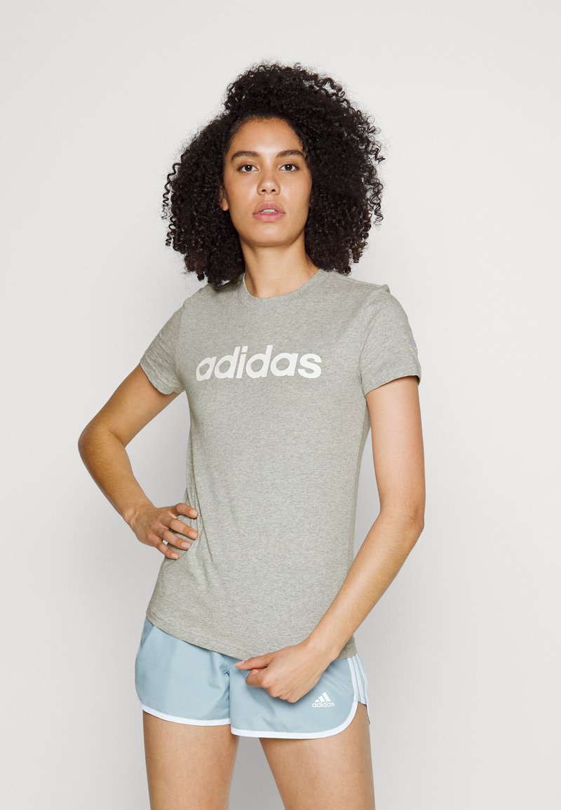 Svetlo šedé tričko s krátkymi rukávmi a okrúhlym výstrihom, s veľkým bielym logom "adidas" na prednej strane. Mäkčená bavlnená zmes.