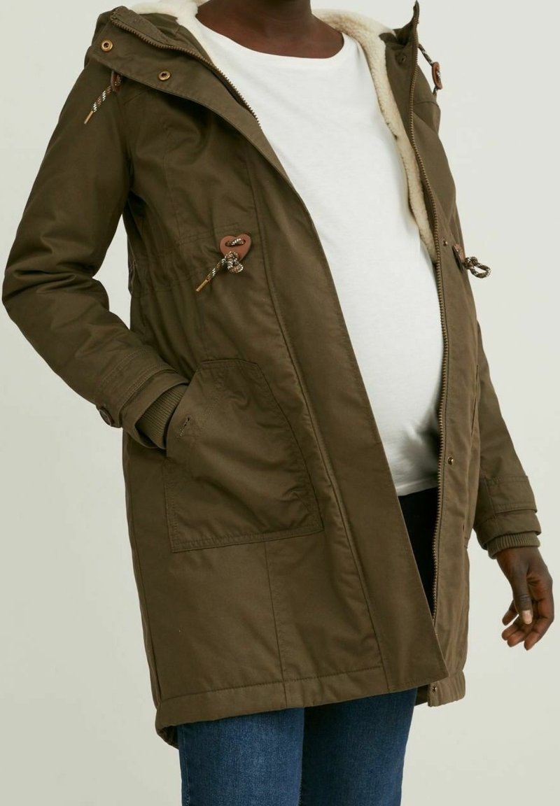 Parka vert olive avec une capuche bordée de fourrure, un cordon de serrage à la taille, deux poches avant et des accents à boutons. Tissu doux et texturé.