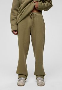 Olijfgroene sweatpants van zachte stof, met een elastische tailleband en trekkoord, wijde pijpen en zijzakken.