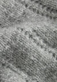 Nahaufnahme von gestricktem grauem Stoff, der eine weiche, strukturierte Oberfläche mit einer Mischung aus hellen und dunklen grauen Fasern zeigt und ein grobes Muster präsentiert.