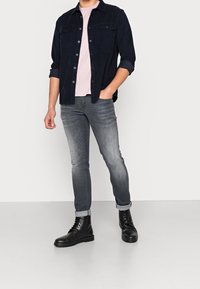 Laivastonsininen napillinen paita, vaaleanpunainen t-paita, harmaat tiimalasihousut ja mustat nyörilliset nilkkurit teksturoidulla pinnalla.