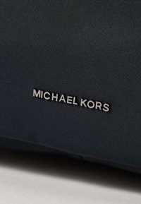 Borsa in nylon nero con superficie testurizzata e logo "MICHAEL KORS" in argento. Il design è elegante con minimi accenti hardware.
