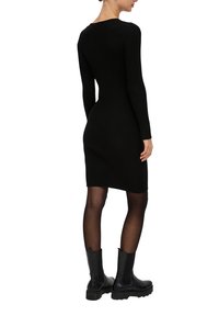 Schwarzes geripptes Strickkleid mit langen Ärmeln und taillierter Silhouette. Kombiniert mit schwarzen Stiefeletten mit dicker Sohle.
