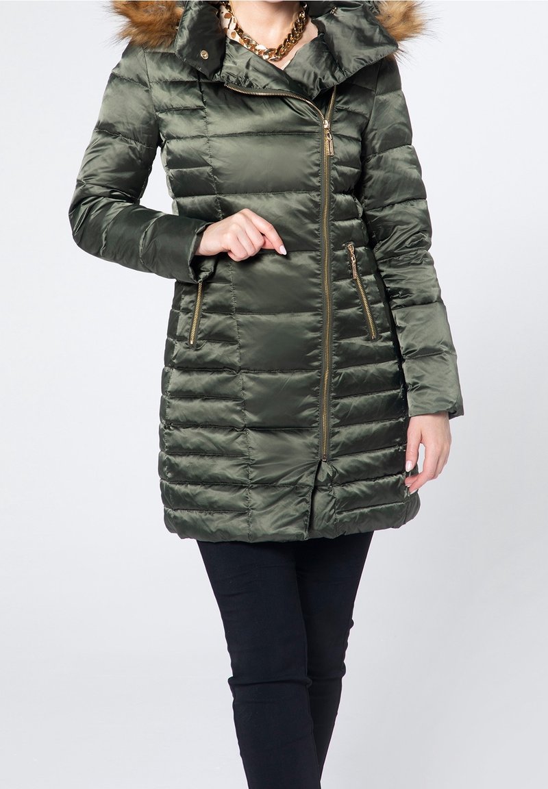 Abrigo acolchado de color verde oliva con capucha con ribete de piel, cierre metálico de cremallera y dos bolsillos con cremallera, con textura acolchada y silueta ajustada.