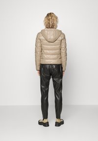 Beżowa kurtka puchowa z kapturem, z pikowanymi sekcjami, w połączeniu z czarnymi skórzanymi spodniami. Stylizację dopełniają beżowe botki za kostkę.