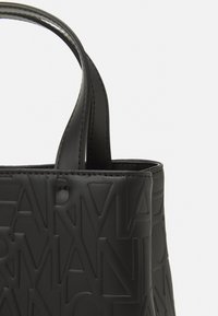 Borsa a spalla nera in pelle con motivo in rilievo del logo, texture liscia e manici doppi resistenti. Design minimalista senza hardware visibile.