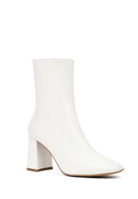 Bottine en cuir blanc avec un bout pointu et un talon bloc. Texture lisse et détails de couture sur les côtés.