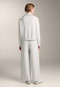 Hellgrauer Strickpullover mit umgeschlagenem Kragen, kombiniert mit passenden, weit geschnittenen Hosen. Weicher Stoff, lässige Passform und minimalistisches Design.
