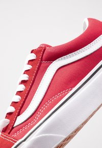 Röd canvas sneakers med vita snören, kontrasterande sidremsa, texturerad gummisula och synliga sömmar.