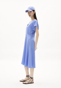 Vestido corto de color azul claro, con mangas cortas y escote en V, falda acampanada y detalles plisados. Combinado con sandalias negras de tiras y una gorra a juego.