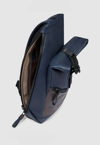 Zaino in pelle blu navy con chiusura a cerniera, dotato di una tasca laterale e tracolla regolabile. Texture liscia con un design elegante e moderno.