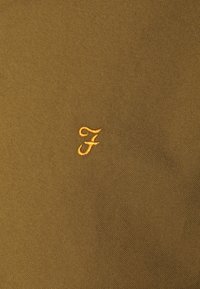 Tessuto verde oliva con una texture liscia, caratterizzato da un piccolo logo giallo "F" ricamato nell'angolo in basso a sinistra.