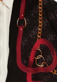 Foulard en soie avec un fond noir orné d'un motif de logo répétitif, des motifs de chaînes bordeaux et dorés, et une finition texturée.