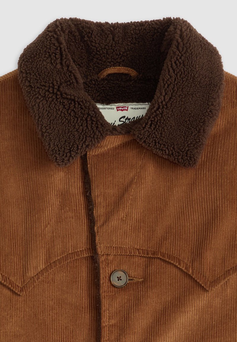 Chaqueta de pana marrón con un cuello de sherpa marrón oscuro, cierre de botones y tejido texturizado, que presenta una etiqueta distintiva de Levi's en su interior.