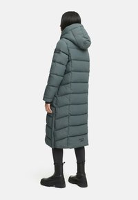 Padded long grey coat with a hood, featuring horizontal quilting, a logo patch on the sleeve, and side slits for ease of movement.