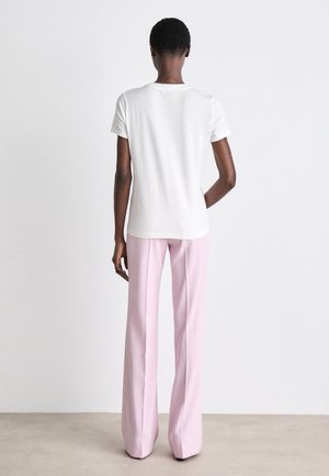 Biała koszulka z krótkim rękawem i różowe spodnie w stylu dzwonów, o gładkiej fakturze i prostym designie. Nogawki spodni są wydłużone, co zapewnia dopasowany wygląd.