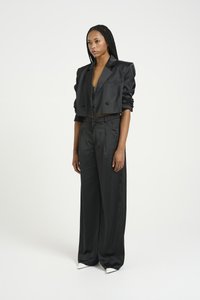 Geknipte zwarte satijnen blazer met twee knopen en opgerolde mouwen, gecombineerd met hoge zwarte broek en puntige witte hakken.