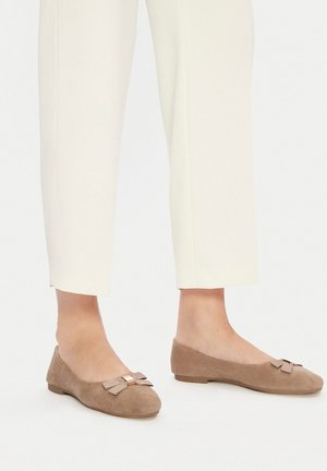 Baleriny zamszowe w jasnobrązowym kolorze z dekoracyjną kokardką i złotym akcentem. Okrągły nosek, niski obcas i gładka tekstura.