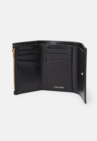 Interiér čiernej koženej peňaženky obsahuje viaceré priehradky na karty, zipsom uzatvorenú časť a zlatý logotyp. Hladká textúra a minimalistický dizajn.