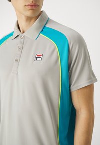 Šedé polo tričko s tyrkysovými akcenty a žlutým lemováním. Má límeček a logo na hrudi. Vyrobeno z texturovaného materiálu.