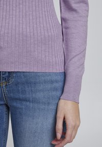 Maglione a coste lavanda con maniche lunghe, realizzato in tessuto morbido. Abbinato a jeans in denim blu con una leggera sfumatura e cuciture arancioni.