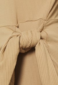 Close-up van een beige ribbelstof geknoopt, met gedetailleerde textuur en stiksels.