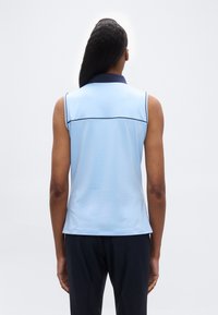 Άτομο που φαίνεται από πίσω φοράει αμάνικο ανοιχτό γαλάζιο πουκάμισο με σκουρόχρωμο γιακά και σκουρόχρωμο παντελόνι, σε απλό λευκό φόντο.