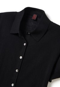 Schwarzes Polo-Shirt mit kurzen Ärmeln und geripptem Kragen, vier weißen Knöpfen und einem roten Etikett mit gesticktem Schriftzug im Kragen.