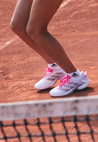 Legs of a tennis player wearing white Adidas shoes with pink laces, standing on a clay court near the net.