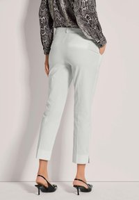 Witte op maat gemaakte broek met een recht model, voorzien van zijzakken en een cropped lengte, gecombineerd met zwarte bandjeshakken en een gemusterd top.